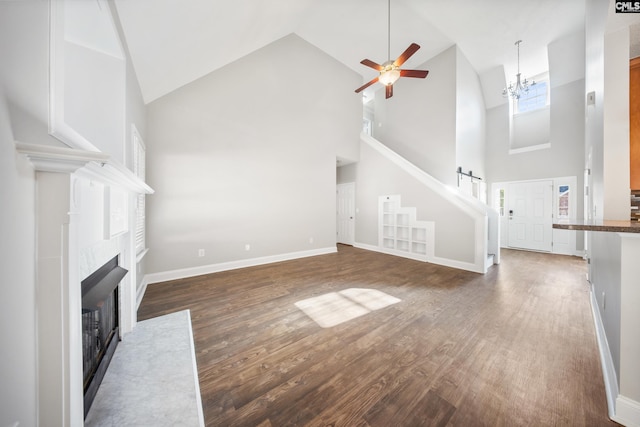 unfurnished living room featuring a tiled fireplace, high vaulted ceiling, dark wood-type flooring, and ceiling fan with notable chandelier