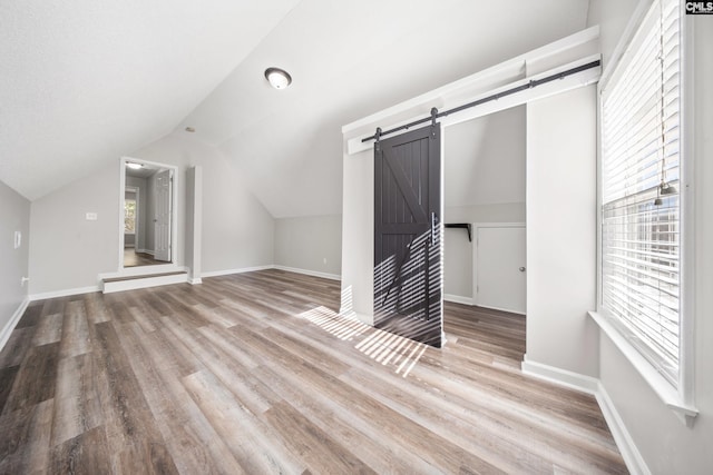 additional living space featuring light wood-type flooring, a barn door, and lofted ceiling