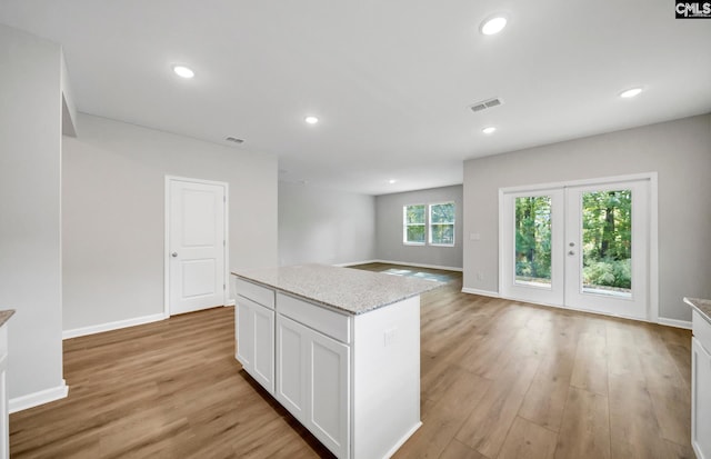 kitchen featuring a center island, french doors, light stone counters, light hardwood / wood-style floors, and white cabinets