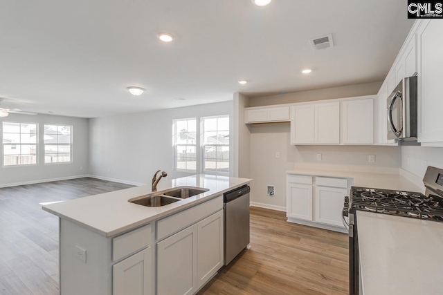 kitchen with white cabinets, appliances with stainless steel finishes, a kitchen island with sink, and sink