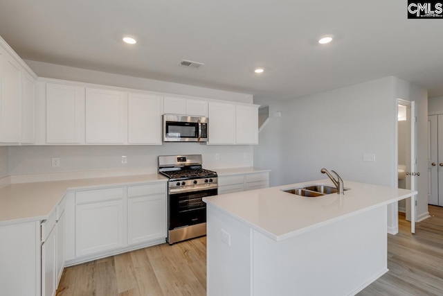 kitchen featuring appliances with stainless steel finishes, light wood-type flooring, a kitchen island with sink, sink, and white cabinets