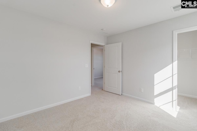 unfurnished bedroom featuring light colored carpet, a walk in closet, and a closet