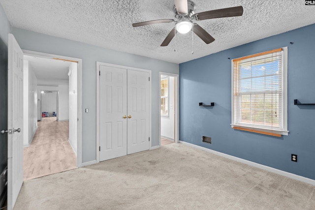 unfurnished bedroom featuring ceiling fan, light colored carpet, a textured ceiling, and a closet