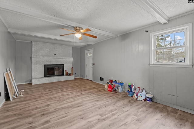 playroom featuring ceiling fan, a brick fireplace, light hardwood / wood-style flooring, beamed ceiling, and a textured ceiling