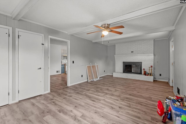 unfurnished living room with beam ceiling, ceiling fan, a textured ceiling, a fireplace, and light wood-type flooring