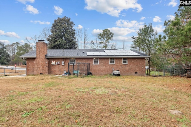 back of house with solar panels and a lawn