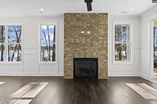 unfurnished living room featuring a fireplace, dark wood-type flooring, ceiling fan, and crown molding