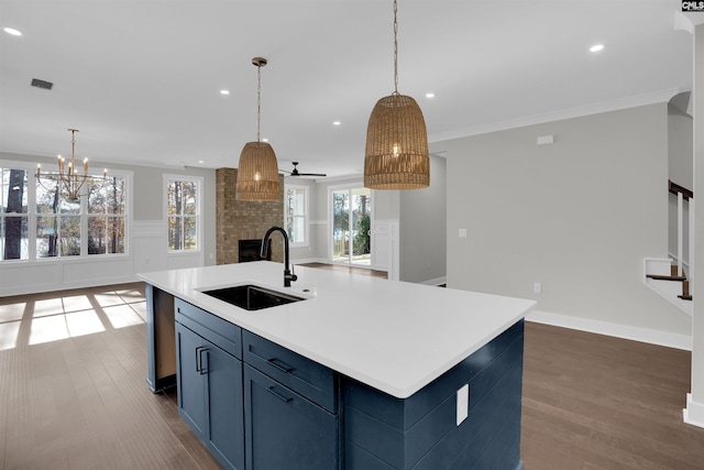 kitchen featuring ceiling fan with notable chandelier, crown molding, sink, an island with sink, and a large fireplace