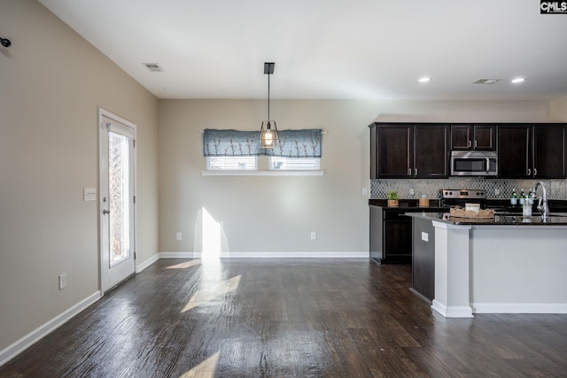 kitchen with hanging light fixtures, stainless steel appliances, dark hardwood / wood-style floors, backsplash, and dark brown cabinets