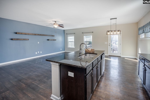 kitchen with dishwasher, sink, dark stone countertops, pendant lighting, and a center island with sink