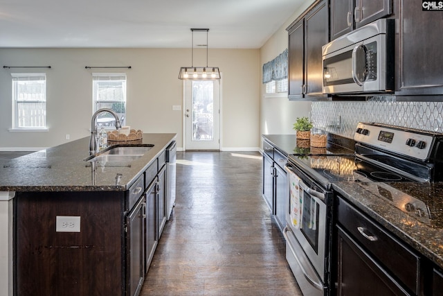 kitchen featuring appliances with stainless steel finishes, backsplash, sink, a center island with sink, and decorative light fixtures