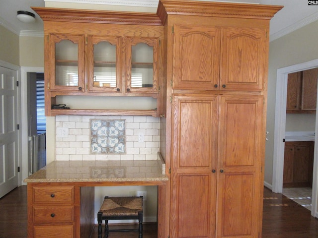 kitchen with light stone countertops, crown molding, built in desk, and dark wood-type flooring