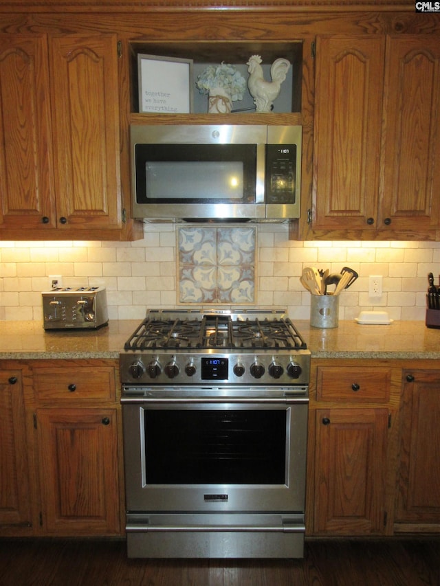 kitchen with appliances with stainless steel finishes, backsplash, light stone counters, and dark wood-type flooring