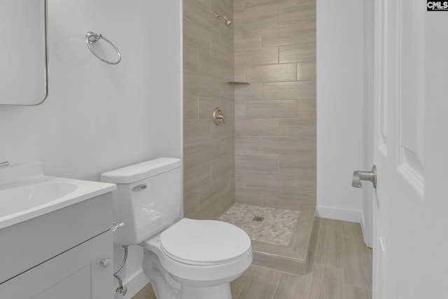 bathroom with a tile shower, vanity, and toilet