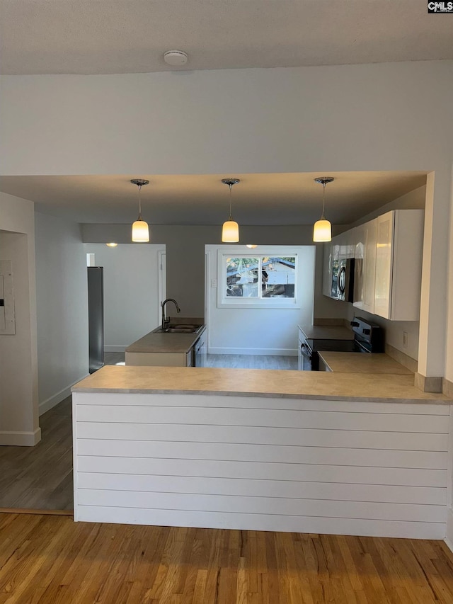 kitchen featuring sink, black / electric stove, kitchen peninsula, pendant lighting, and light wood-type flooring