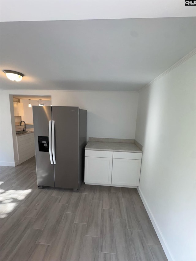 kitchen with sink, light hardwood / wood-style flooring, stainless steel fridge, white cabinets, and ornamental molding