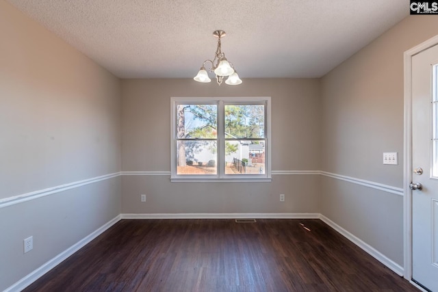 empty room featuring dark hardwood / wood-style flooring, a textured ceiling, and a chandelier