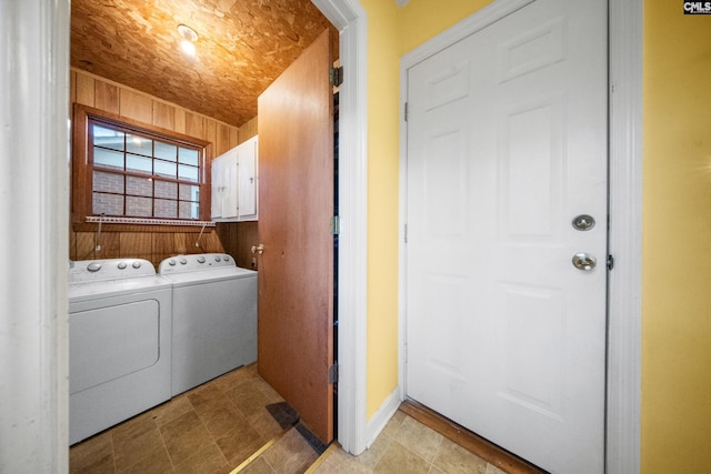 clothes washing area featuring washer and dryer, cabinets, and wooden walls