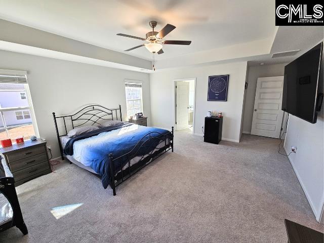 carpeted bedroom with ensuite bath, a tray ceiling, baseboards, and ceiling fan