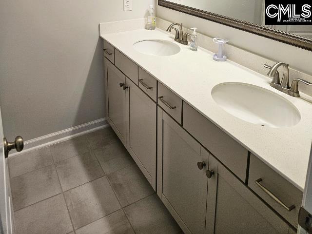 bathroom featuring a sink, baseboards, double vanity, and tile patterned floors