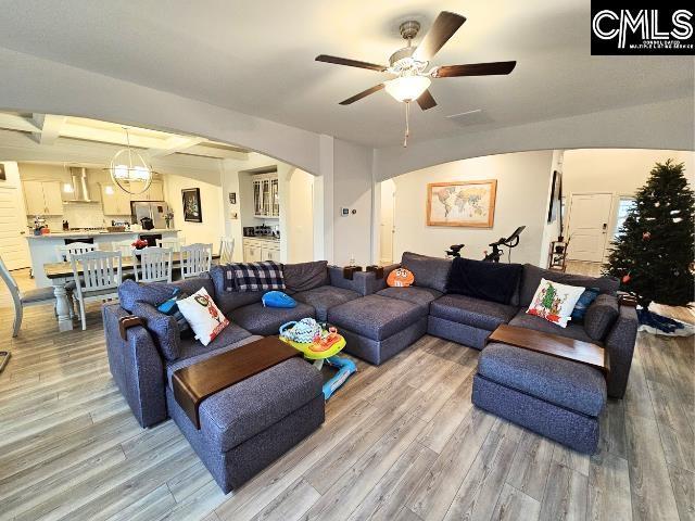 living room featuring arched walkways, light wood-style floors, and ceiling fan