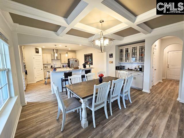 dining area featuring arched walkways, a notable chandelier, beam ceiling, and wood finished floors