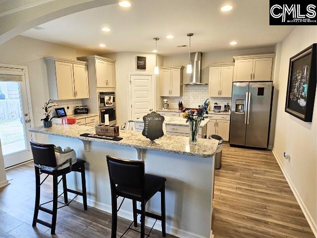 kitchen with wall chimney range hood, stainless steel fridge with ice dispenser, a breakfast bar, dark wood-style floors, and arched walkways