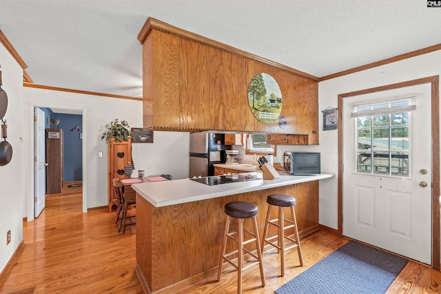 kitchen with stainless steel fridge, light wood-type flooring, kitchen peninsula, and black electric cooktop