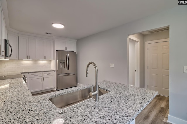 kitchen with decorative backsplash, light stone counters, sink, stainless steel fridge with ice dispenser, and white cabinetry