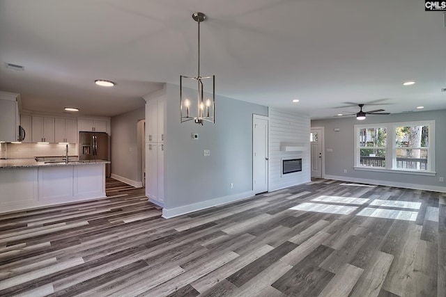 unfurnished living room featuring ceiling fan with notable chandelier, a large fireplace, light hardwood / wood-style floors, and sink