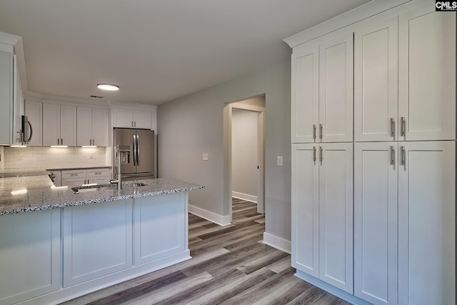 kitchen featuring backsplash, kitchen peninsula, stainless steel fridge with ice dispenser, light stone counters, and white cabinetry