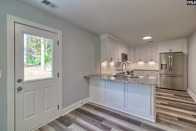 kitchen with light stone countertops, backsplash, stainless steel appliances, sink, and white cabinets