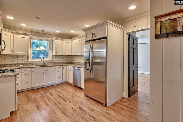 kitchen with appliances with stainless steel finishes, ornamental molding, sink, decorative light fixtures, and light hardwood / wood-style flooring