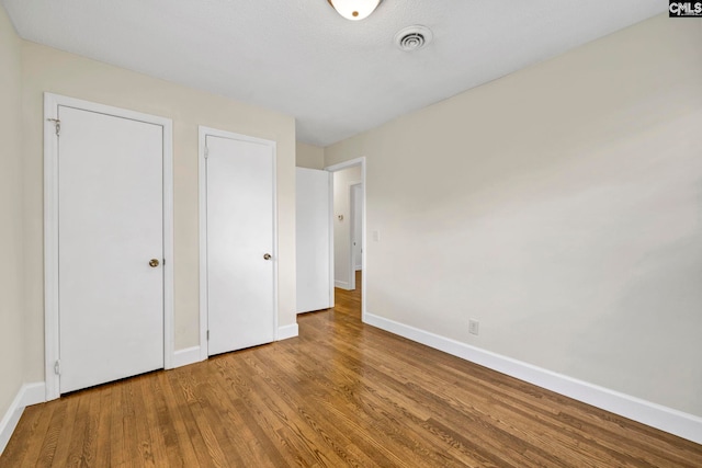 unfurnished bedroom with wood-type flooring and two closets