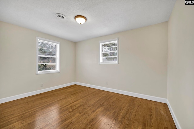 spare room featuring a healthy amount of sunlight, wood-type flooring, and a textured ceiling