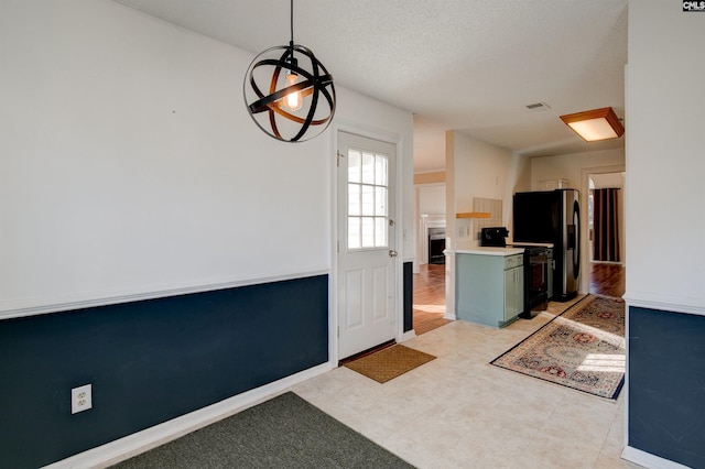 interior space featuring pendant lighting, black electric range oven, stainless steel refrigerator with ice dispenser, and a textured ceiling