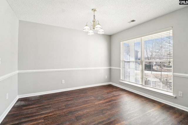 spare room featuring dark hardwood / wood-style floors, a chandelier, and a textured ceiling