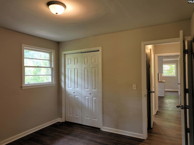 unfurnished bedroom with multiple windows, a closet, and dark wood-type flooring