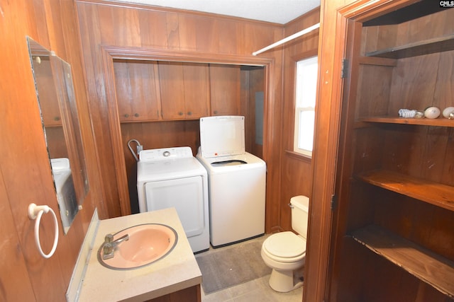 clothes washing area with wood walls, washer and clothes dryer, light tile patterned floors, and sink