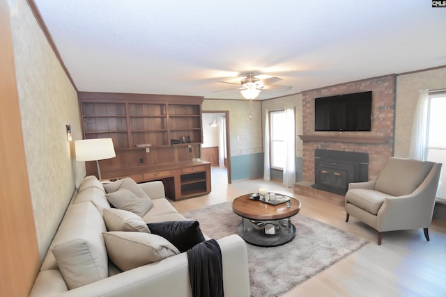 living room with a wood stove, ceiling fan, light hardwood / wood-style flooring, crown molding, and a textured ceiling