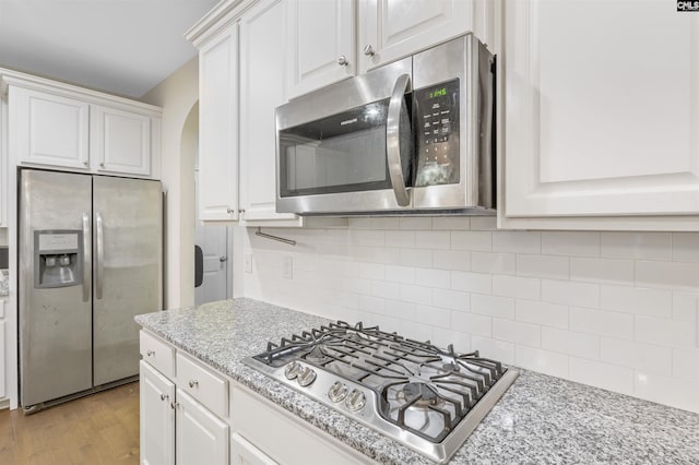 kitchen with decorative backsplash, appliances with stainless steel finishes, light wood-type flooring, light stone countertops, and white cabinetry