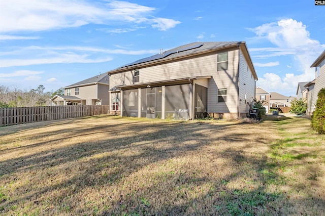 rear view of house with solar panels, a lawn, and a sunroom