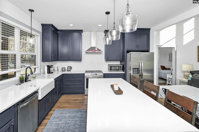 kitchen featuring sink, hanging light fixtures, stainless steel appliances, wall chimney range hood, and dark hardwood / wood-style flooring