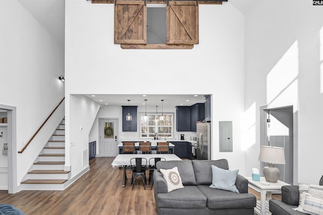 living room featuring dark wood-type flooring, electric panel, sink, a barn door, and a towering ceiling