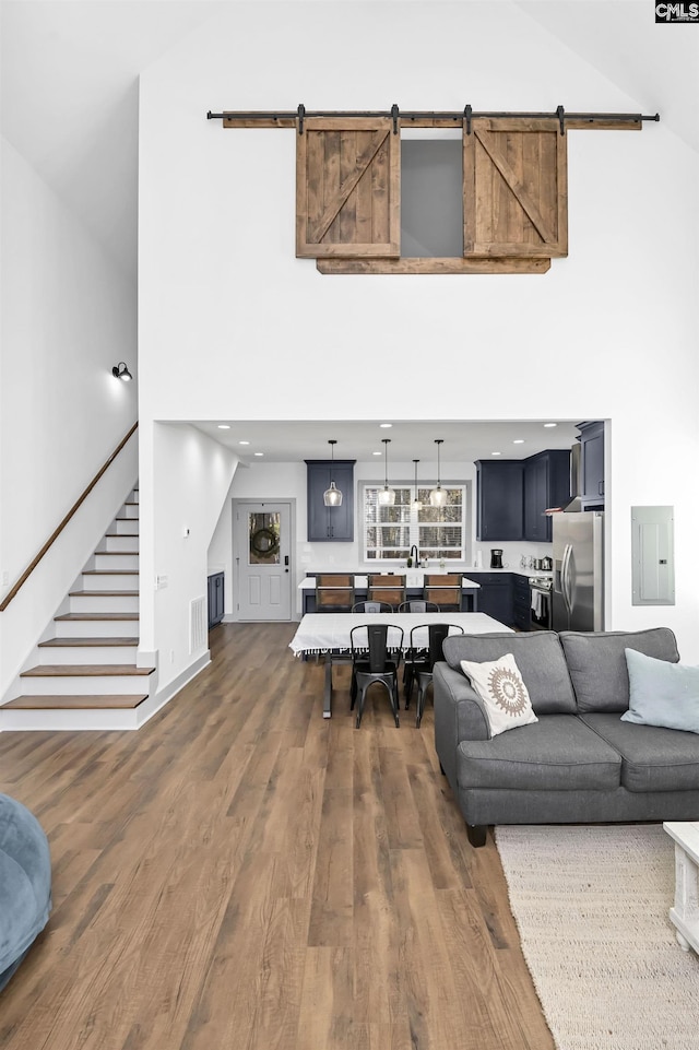 living room featuring a towering ceiling, a barn door, electric panel, and dark wood-type flooring