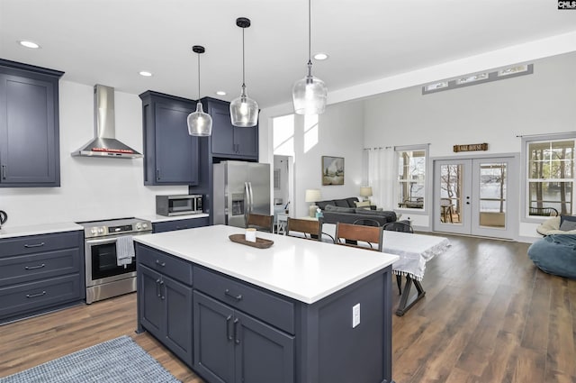 kitchen with french doors, wall chimney exhaust hood, decorative light fixtures, a kitchen island, and appliances with stainless steel finishes