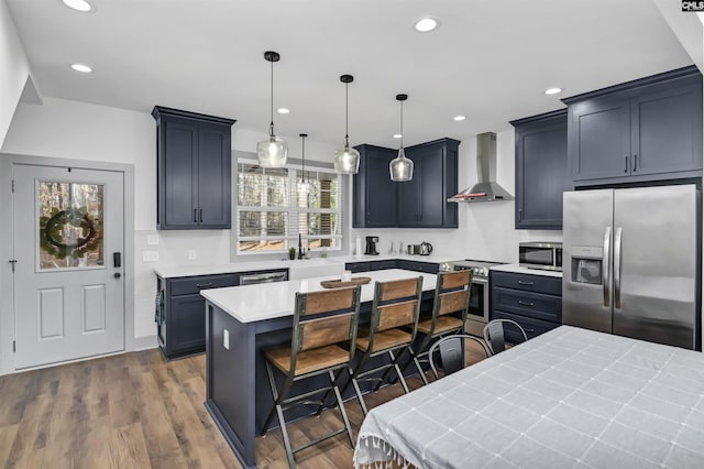 kitchen featuring pendant lighting, a kitchen breakfast bar, wall chimney exhaust hood, appliances with stainless steel finishes, and a kitchen island