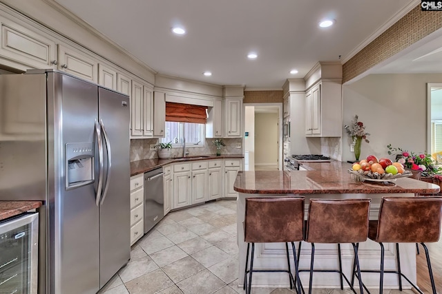 kitchen with sink, wine cooler, kitchen peninsula, a breakfast bar area, and appliances with stainless steel finishes