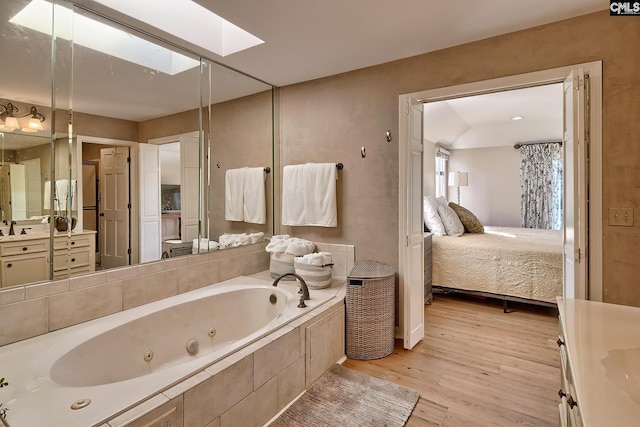 bathroom featuring hardwood / wood-style floors, vanity, a relaxing tiled tub, and a skylight