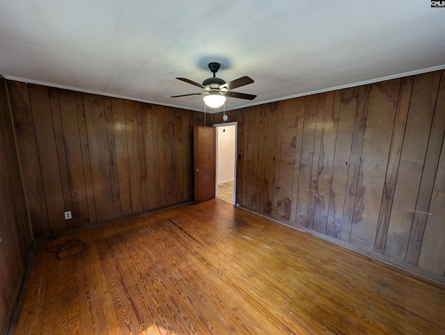 spare room featuring ceiling fan, light wood-type flooring, and wooden walls